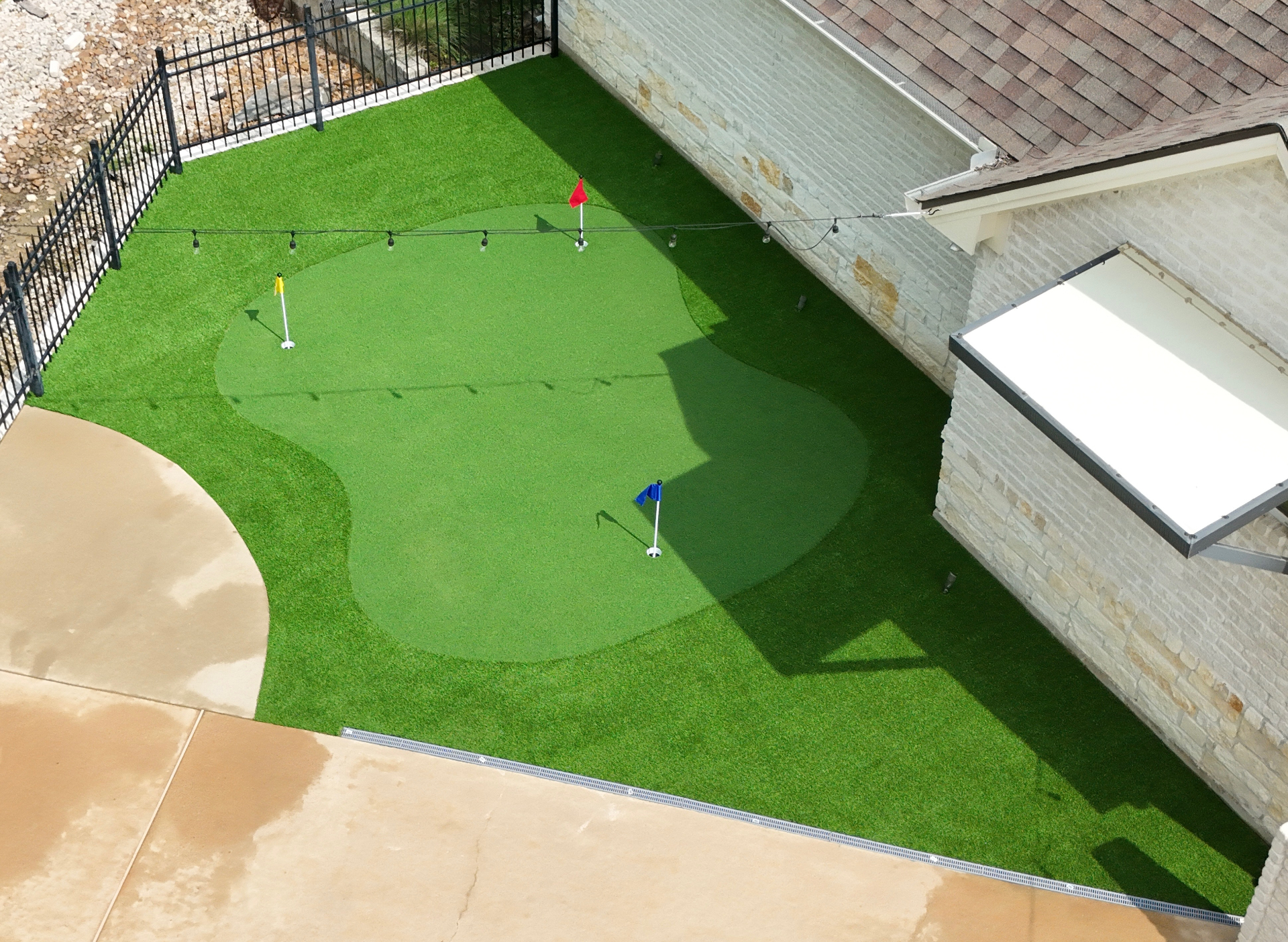 Backyard putting green with red, yellow and blue flags next to stone home