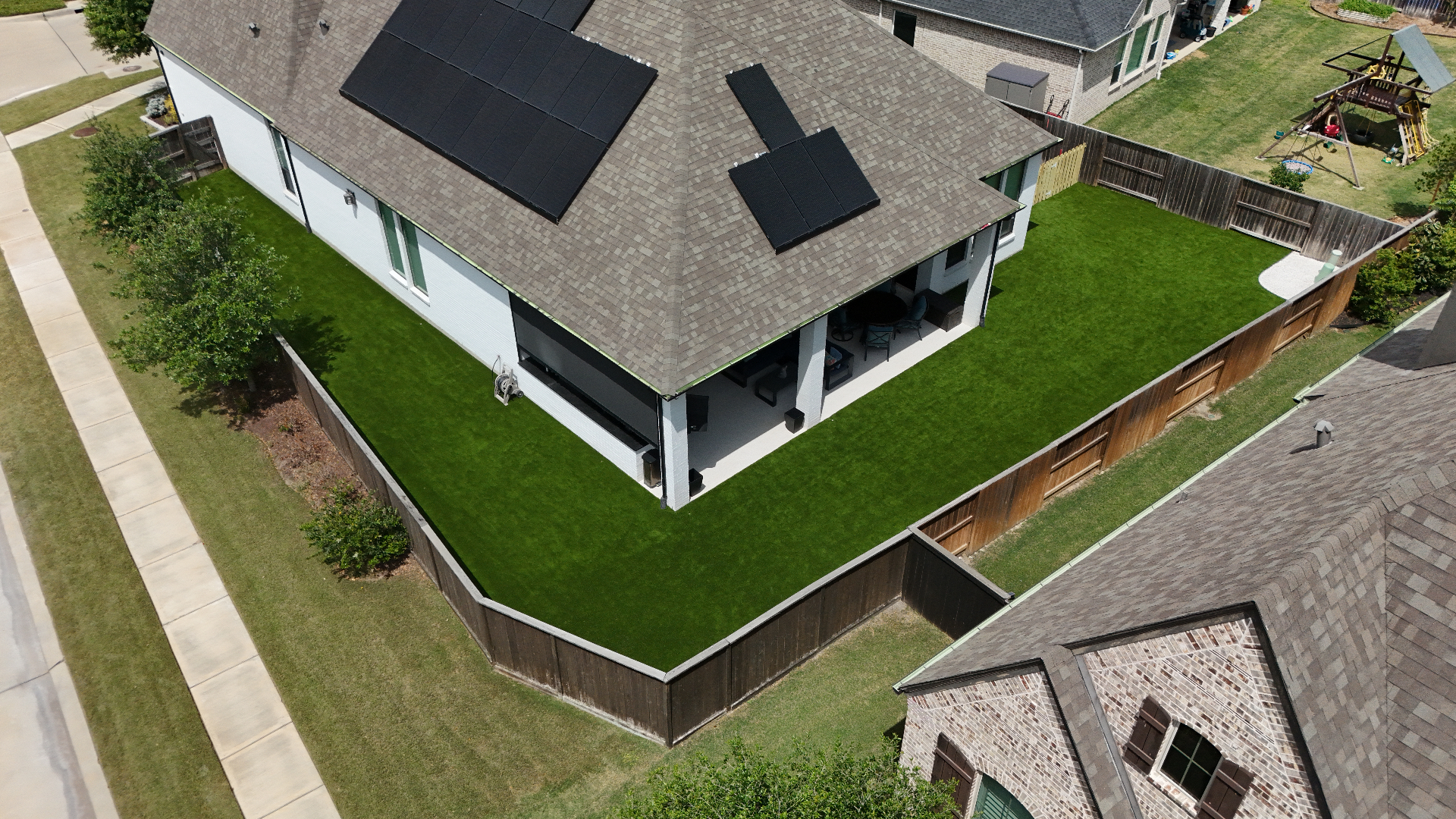 Aerial view of large residential backyard wrapped in artificial turf around covered patio